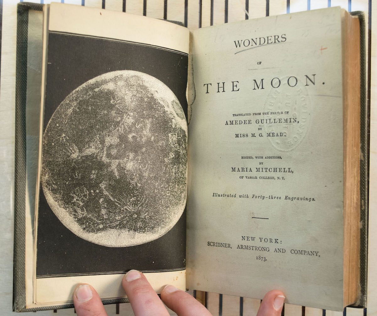 Photo of the title page spread from 'Wonders of the Moon.' The left page has a large, detailed image of the moon in a black sky, and the right page lists the book's title and publication info.